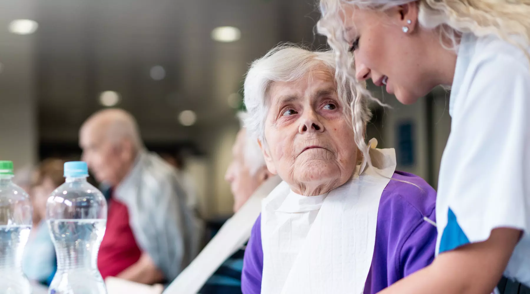Photo d'une dame à table. Elle regarde l'infirmière en train de lui parler