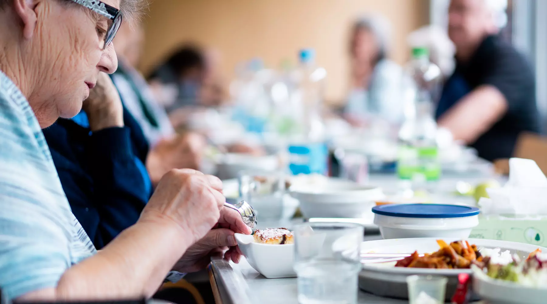 Photo d'une dame en train de manger, d'autres personnes sont visibles à l'arrière-plan, un peu flou
