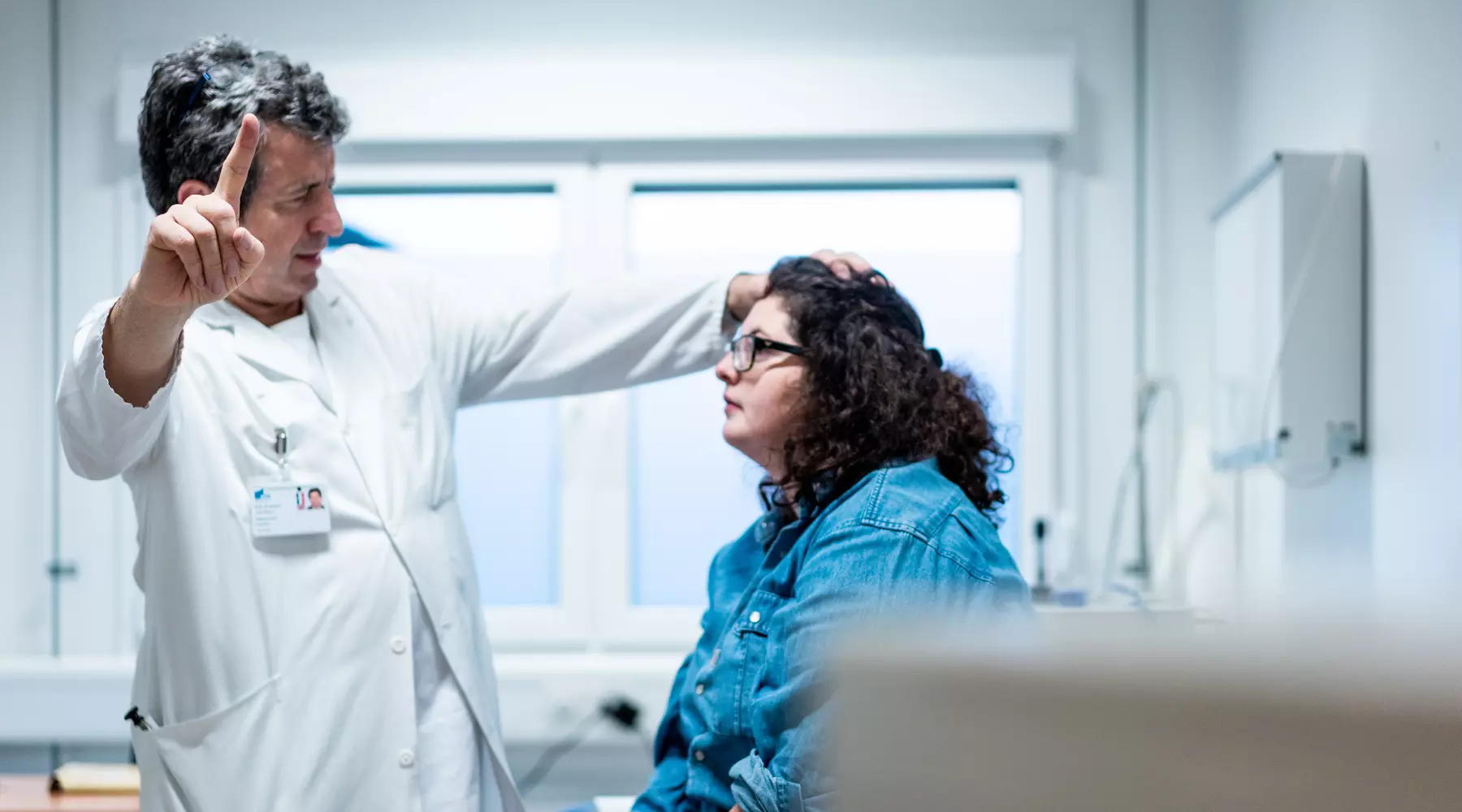 Examen neurologique: une patiente assise suit du regard le doigt du médecin, debout face à elle. 