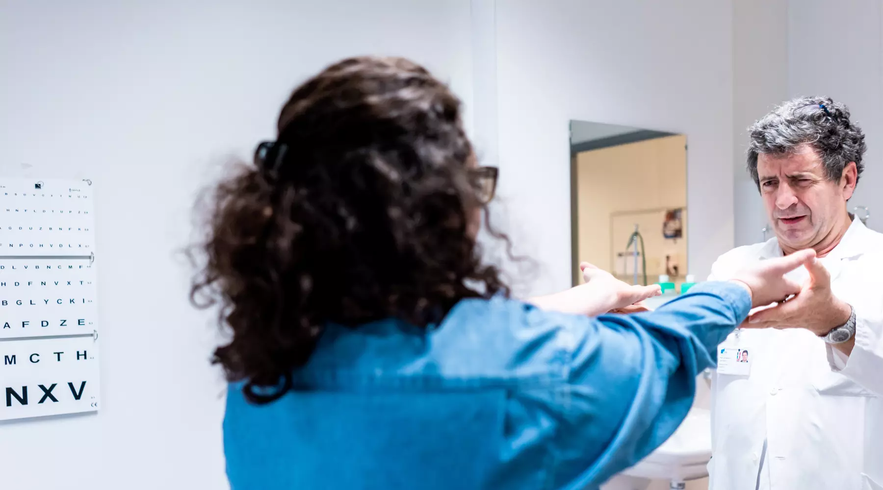 Une patiente vue de dos tend ses deux bras en avant, un médecin la soutient