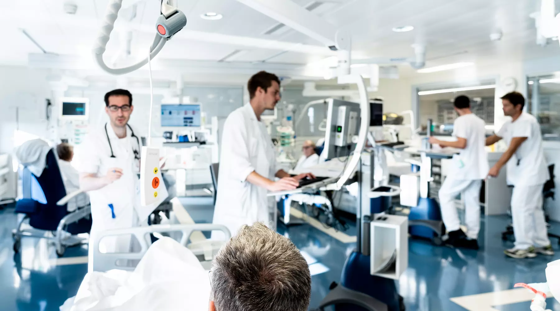 Le personnel médical-soignant s'active dans une pièces des soins intensifs, entre les appareils et deux patients. La pièce est baignée de lumière et dégage du calme, malgré l'activité ambiante.
