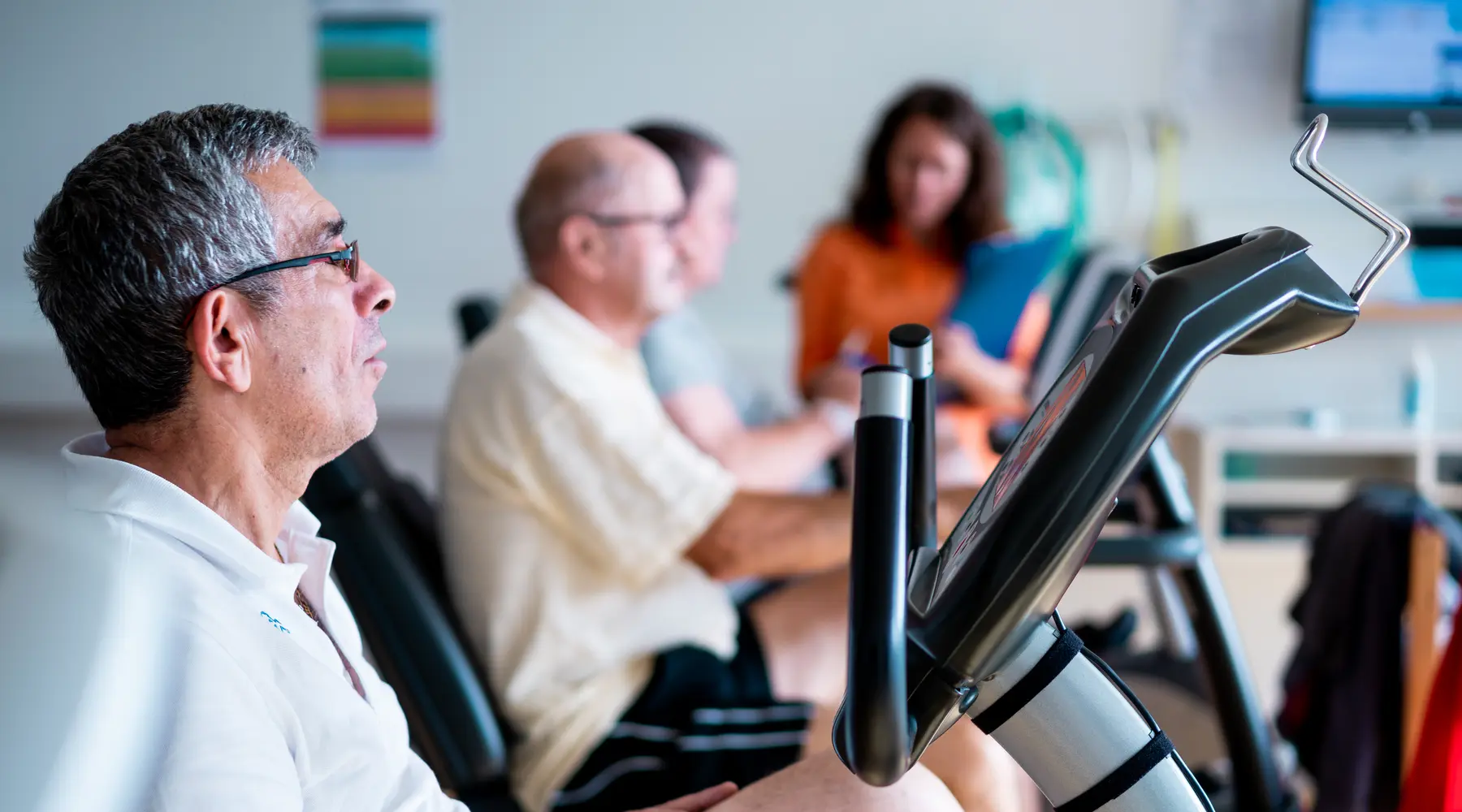 Des patients s'entraînent sur des vélos d'intérieur, sous la supervision d'une physiothérapeute