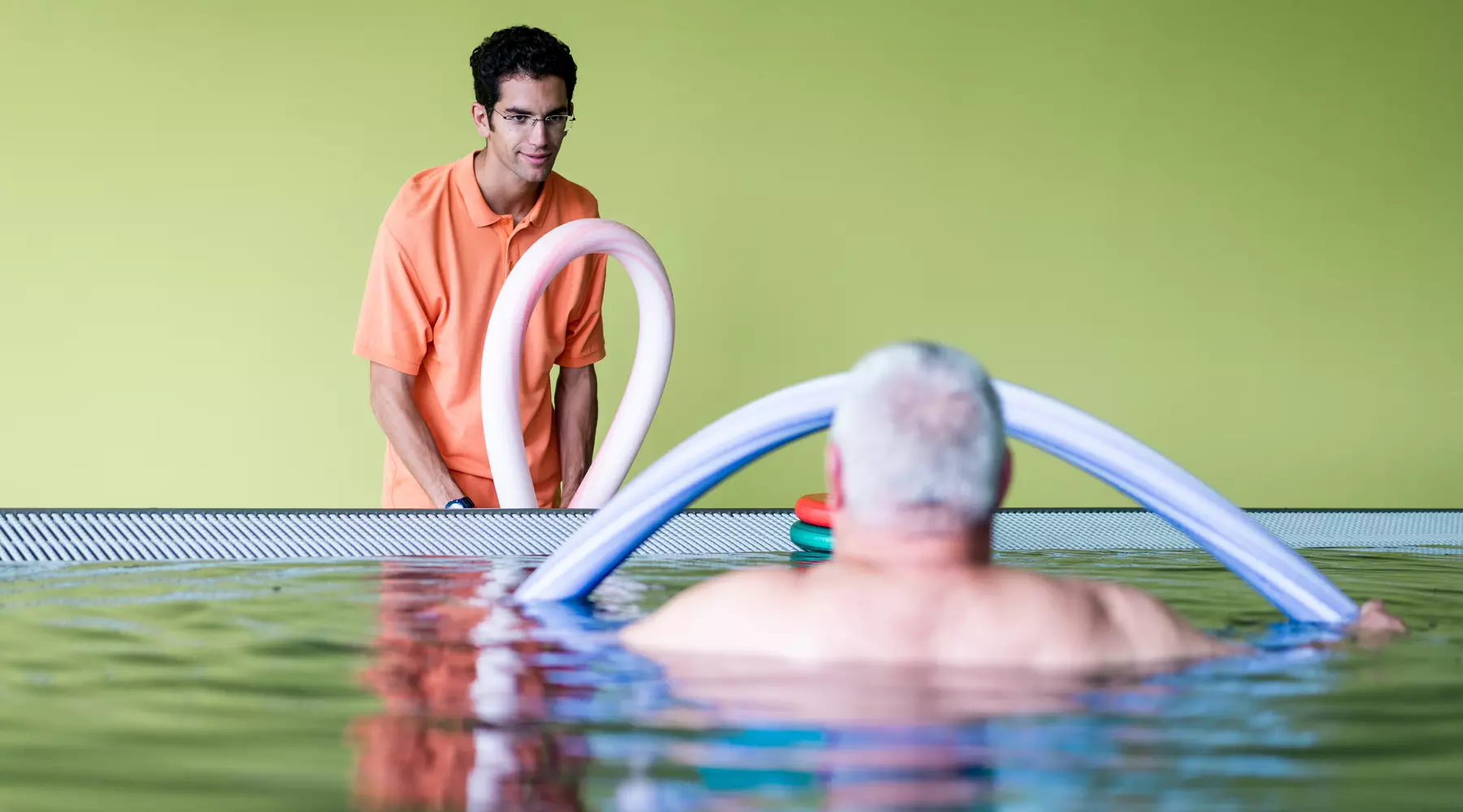 Un physiothérapeute, debout à côté de la piscine thérapeutique, donne des indications à un patient dans l'eau.