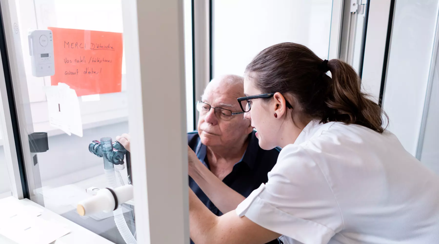 Un médecin explique l'un examen fonctionnel respiratoire à un patient assis face à une machine. 