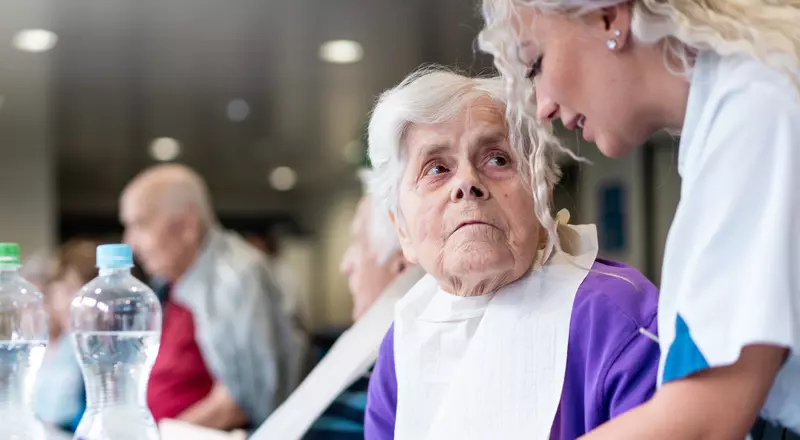 Photo d'une dame à table. Elle regarde l'infirmière en train de lui parler