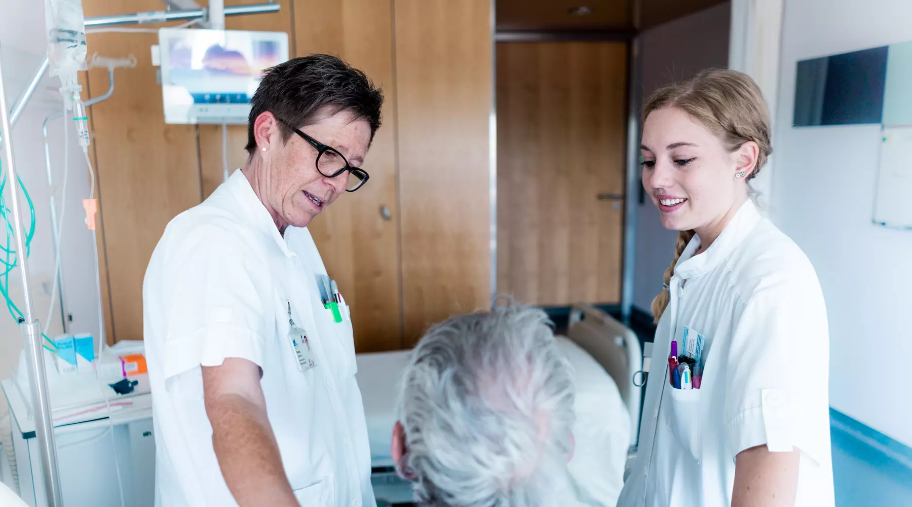 Un patient vu de dos en train de discuter avec deux infirmières, l'une a posé une main sur son épaule.