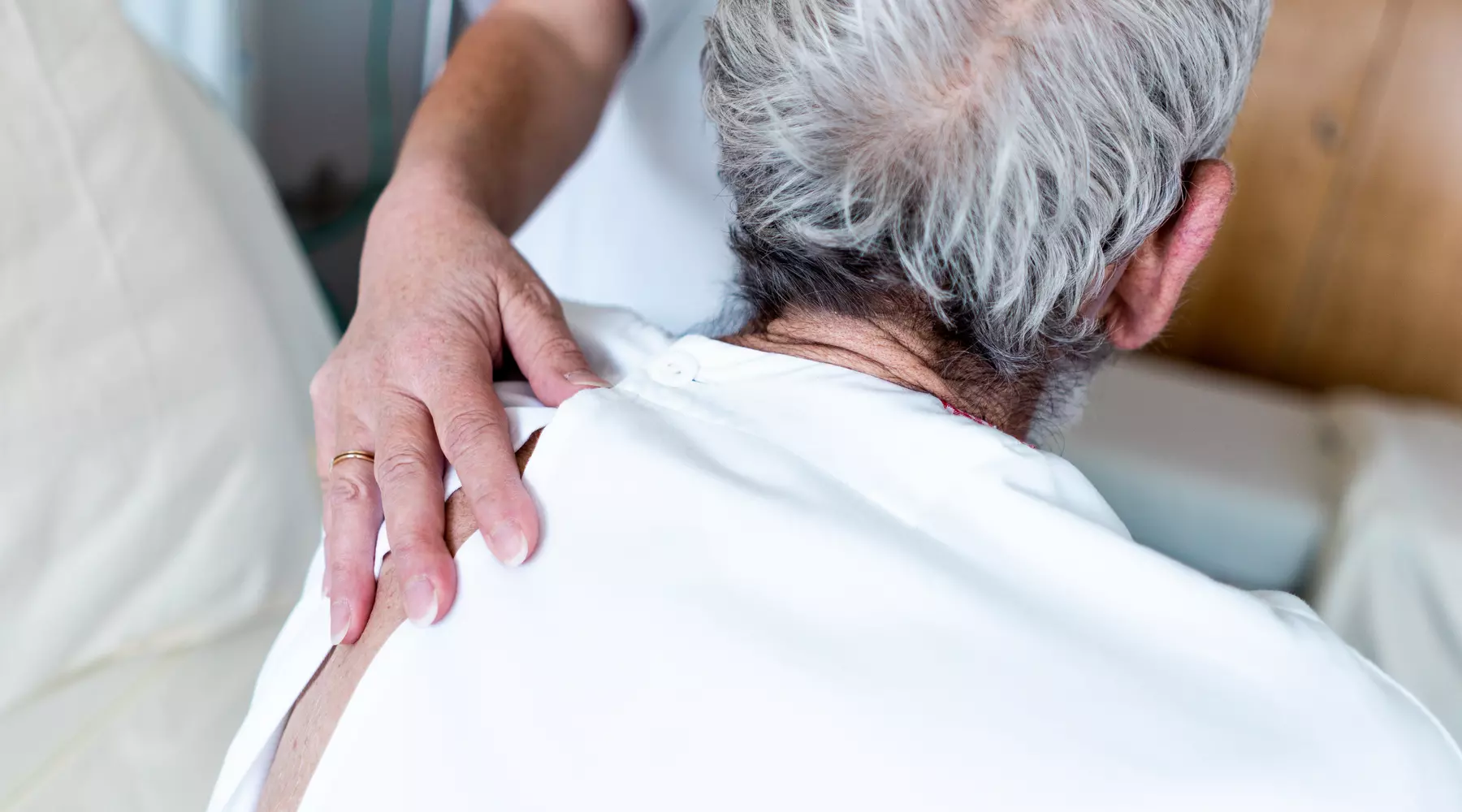 Gros plan sur la main d'une infirmière, délicatement posée sur le dos d'un patient âgé. 