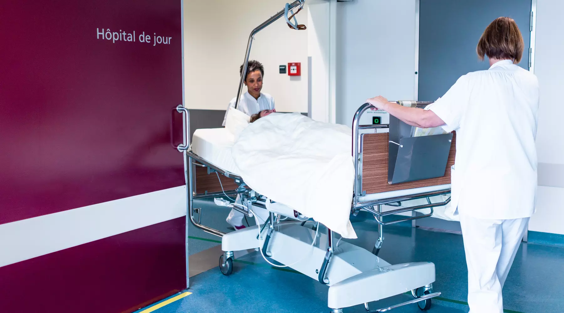 Deux infirmières déplacent un patient dans un lit médicalisé