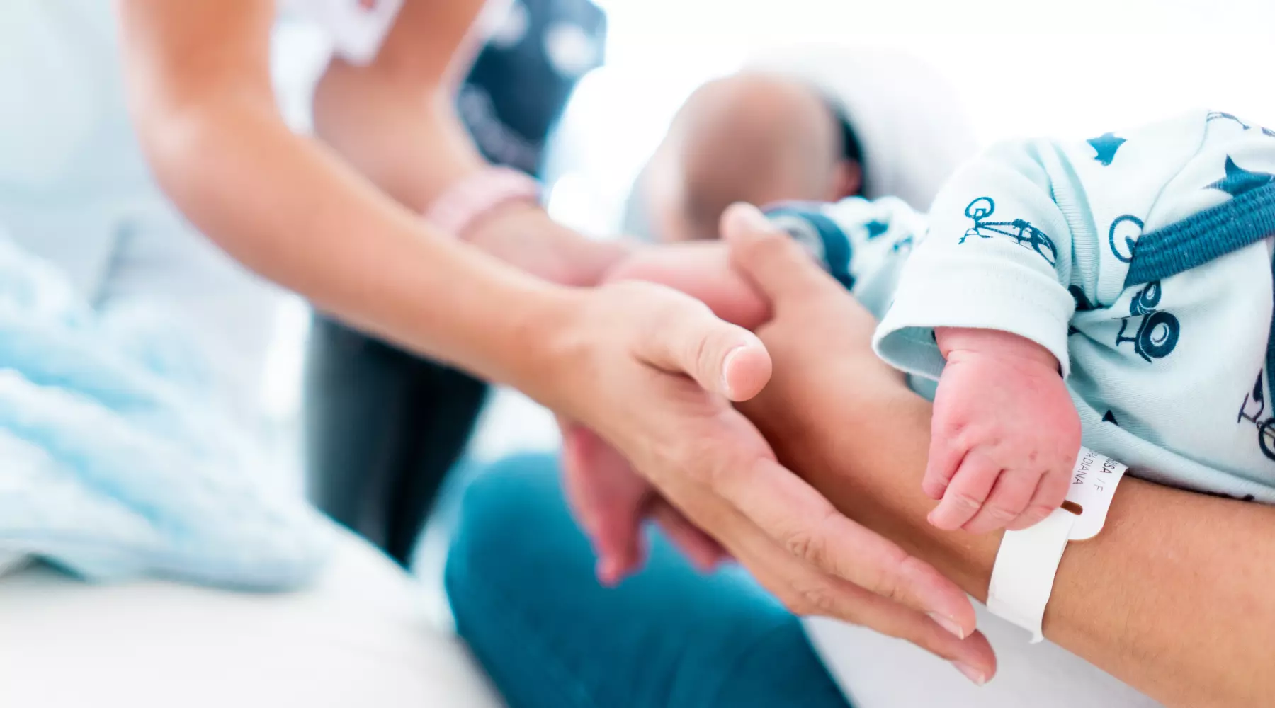 Gros plan sur les mains de la sage-femme qui soutiennent celles de la maman en train de tenir son bébé.