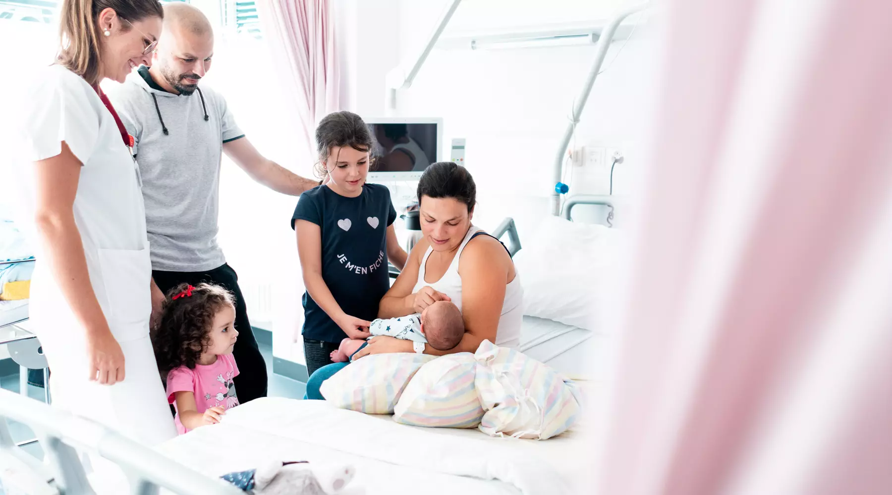 Photo d'une maman assise sur son lit, son nouveau-né dans les bras, entourée par sa famille et une sage-femme.
