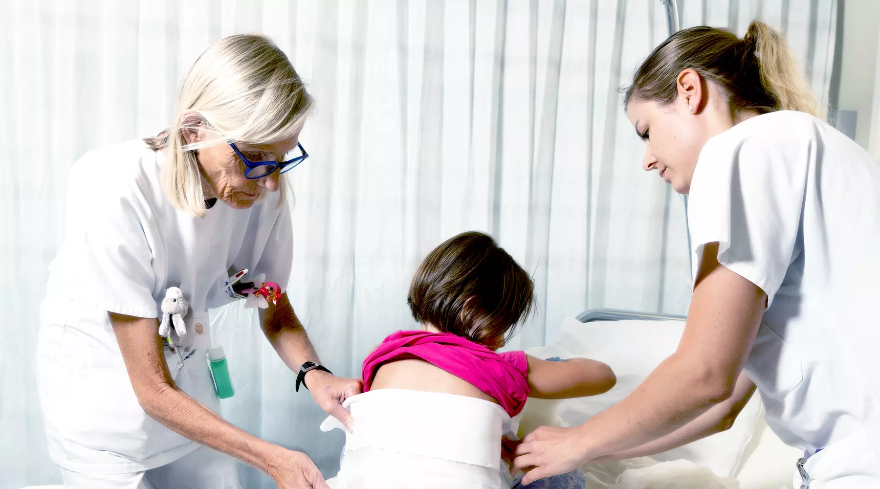 Deux infirmières appliquent un enveloppement à une petite fille assise sur un lit. 