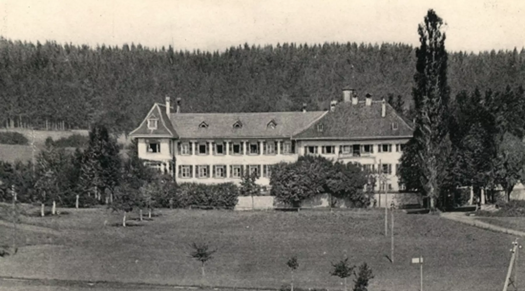 Aussenansicht des Hospiz Billens ca. 1930 in Schwarz-Weiss. Das Gebäude steht zwischen einem Wald und einem Obstgarten. 