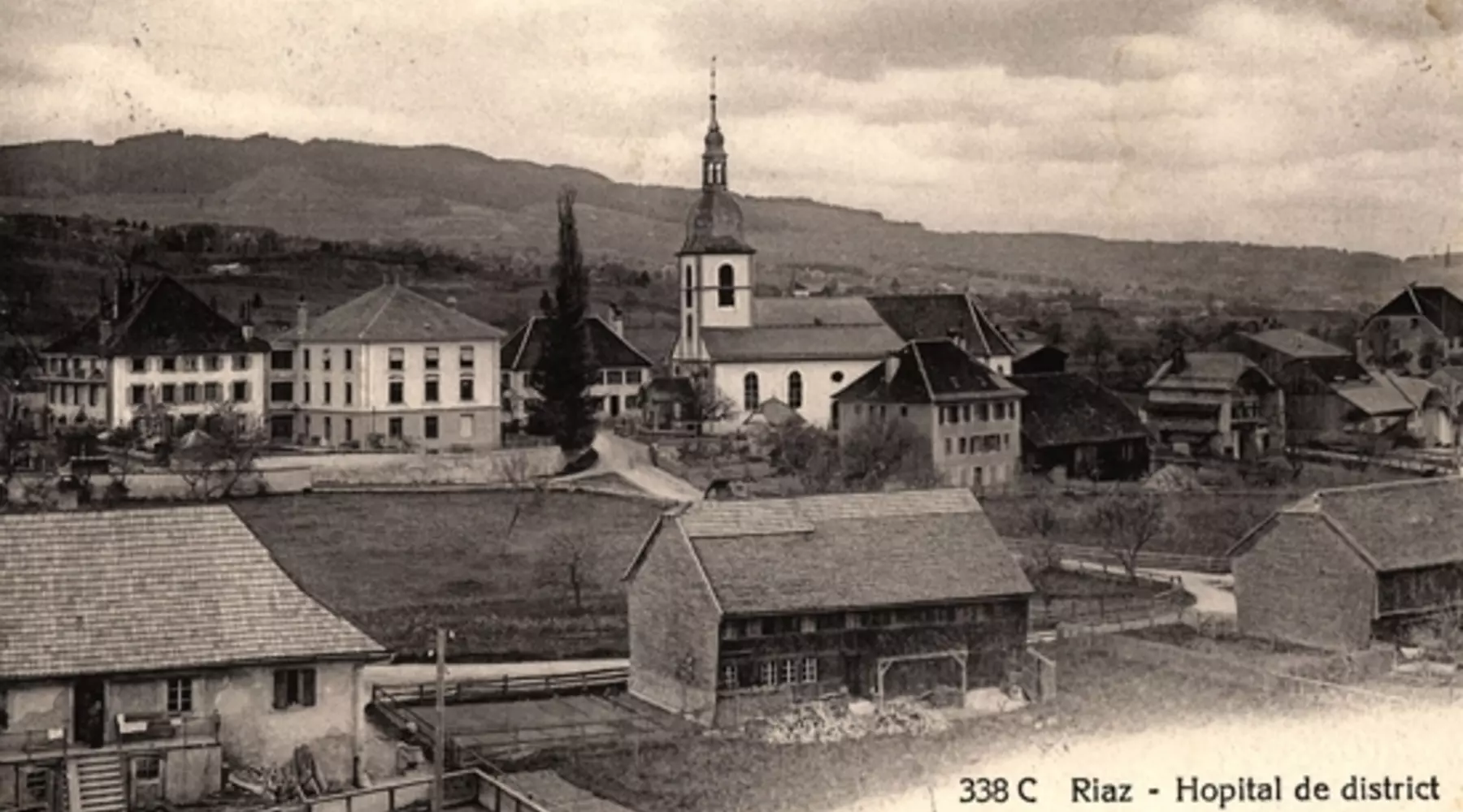 Schwarzweissfoto des Bezirksspitals Riaz ca. 1905. Zu sehen sind mehrere Gebäude, darunter die Kirche. 