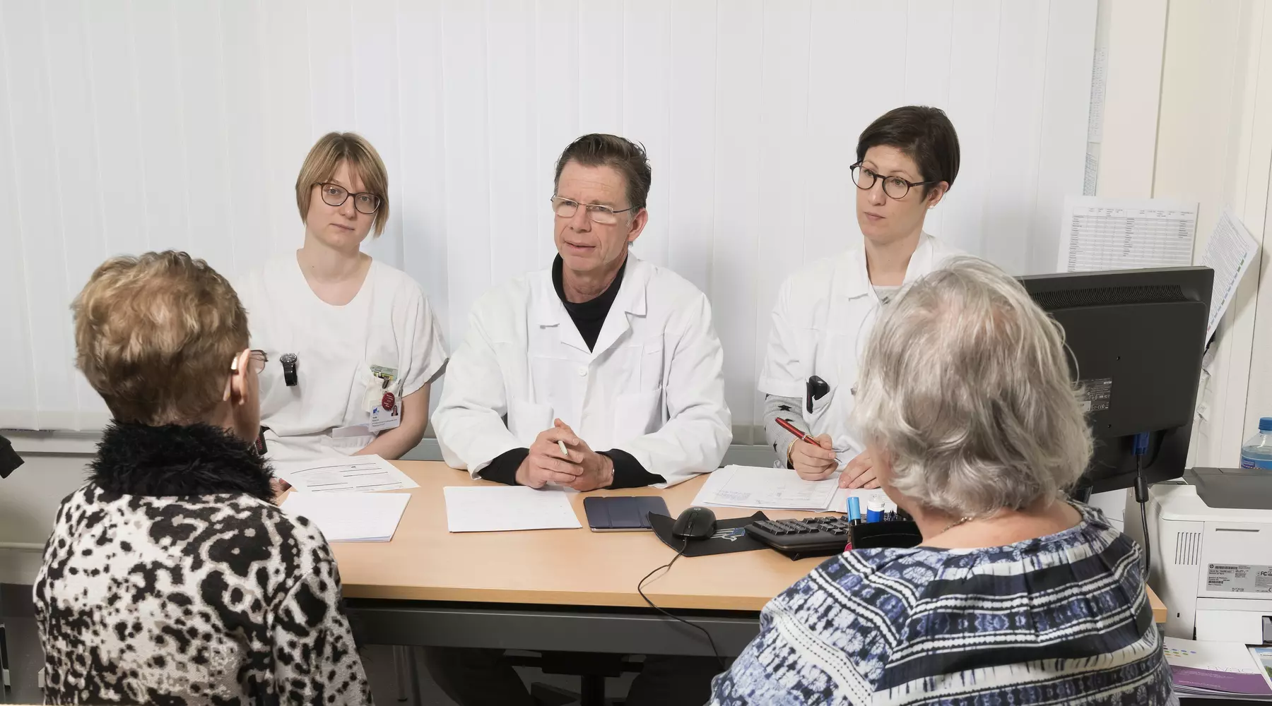 Ärzte und Pflegende unterhalten sich mit zwei älteren Patientinnen