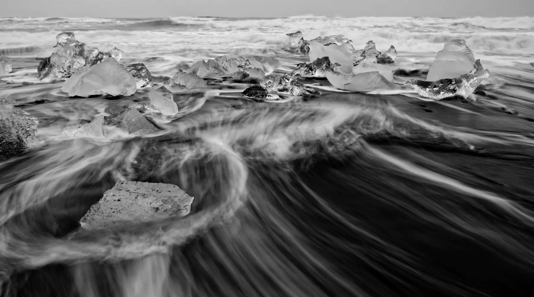 Schwarzweissfoto: Wellen rauschen über Steine und Eisblöcke