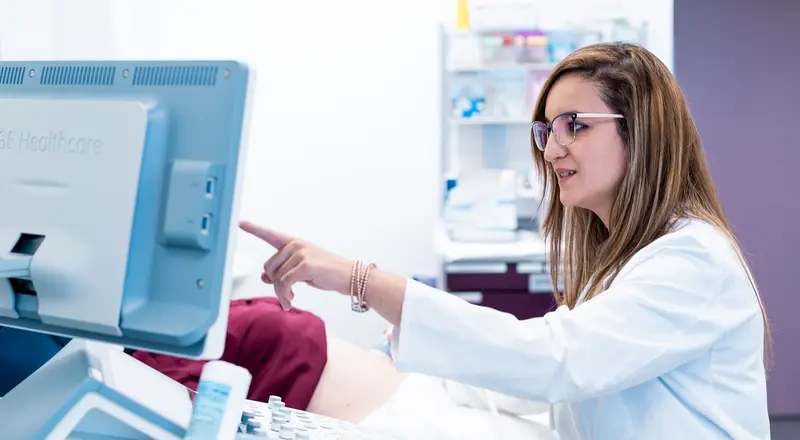 Photo d'une gynécologue en train d'effectuer une échographie. Elle pointe du doigt une information sur un écran d'ordinateur.