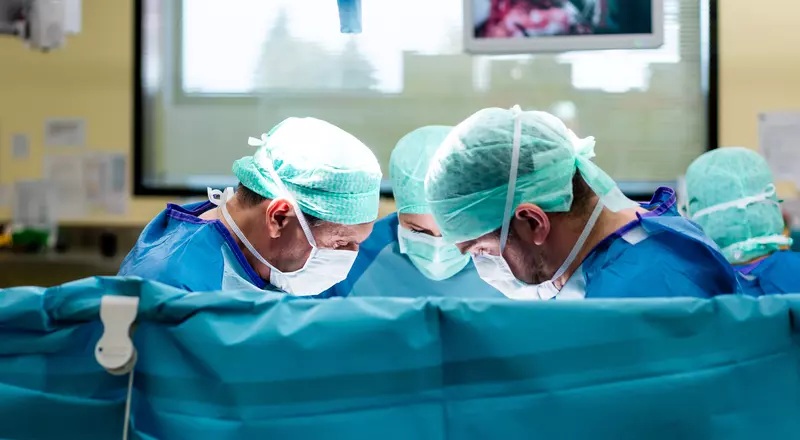 Photo d'une salle d'opération: trois chirurgiens s'affairent derrière un champ opératoire