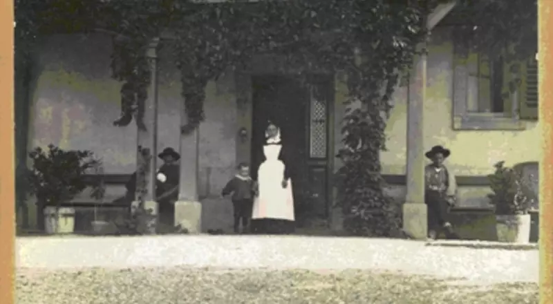 Photo de 1895 dévoilant  l’entrée de l’Hôpital Bon Vouloir, avec une Sœur donnant la main à un enfant  et deux hommes assis sur des banc accolés au mur. 