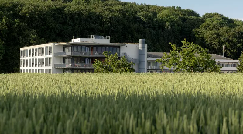 Vue extérieure de l’HFR Tafers, entre la forêt de Maggenberg et un champ, été 2018 