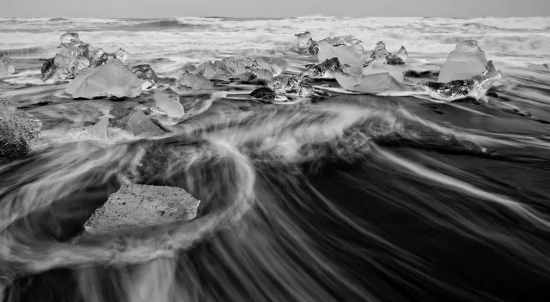 Schwarzweissfoto: Wellen rauschen über Steine und Eisblöcke