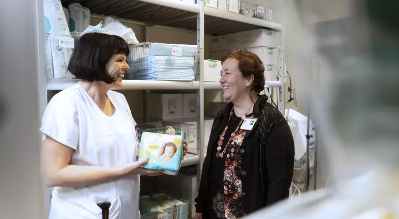 Deux collaboratrices du service d'achat discutent entre les étagères chargées matériel médical
