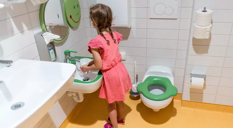 Une petite fille se lave les mains dans les toilettes adaptées à la taille des enfants