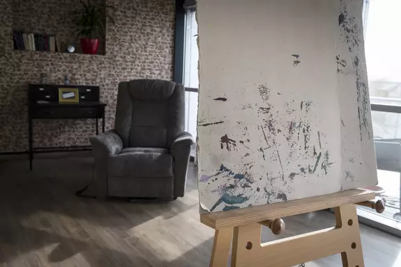 Un chevalet à l'avant-plan, un fauteuil confortable à l'arrière-plan. La toile attend l'arrivée du peintre et son modèle